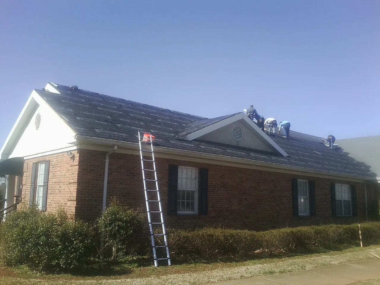 Crew tearing shingles off a brick ranch roof with a ladder set — Emergency Roof Repair work by our crew in Dover