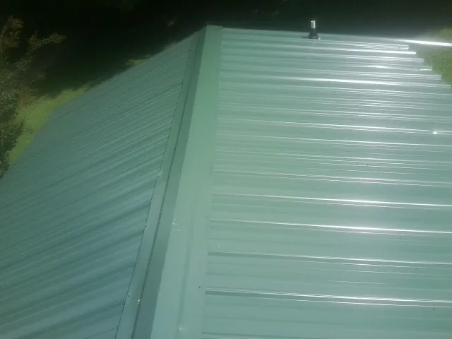 New green metal panels meeting at the ridge of a roof — Flat Roof Repair work by our crew in Dover
